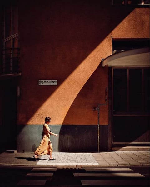 A lone figure walking past a terracotta wall cut by a diagonal shadow