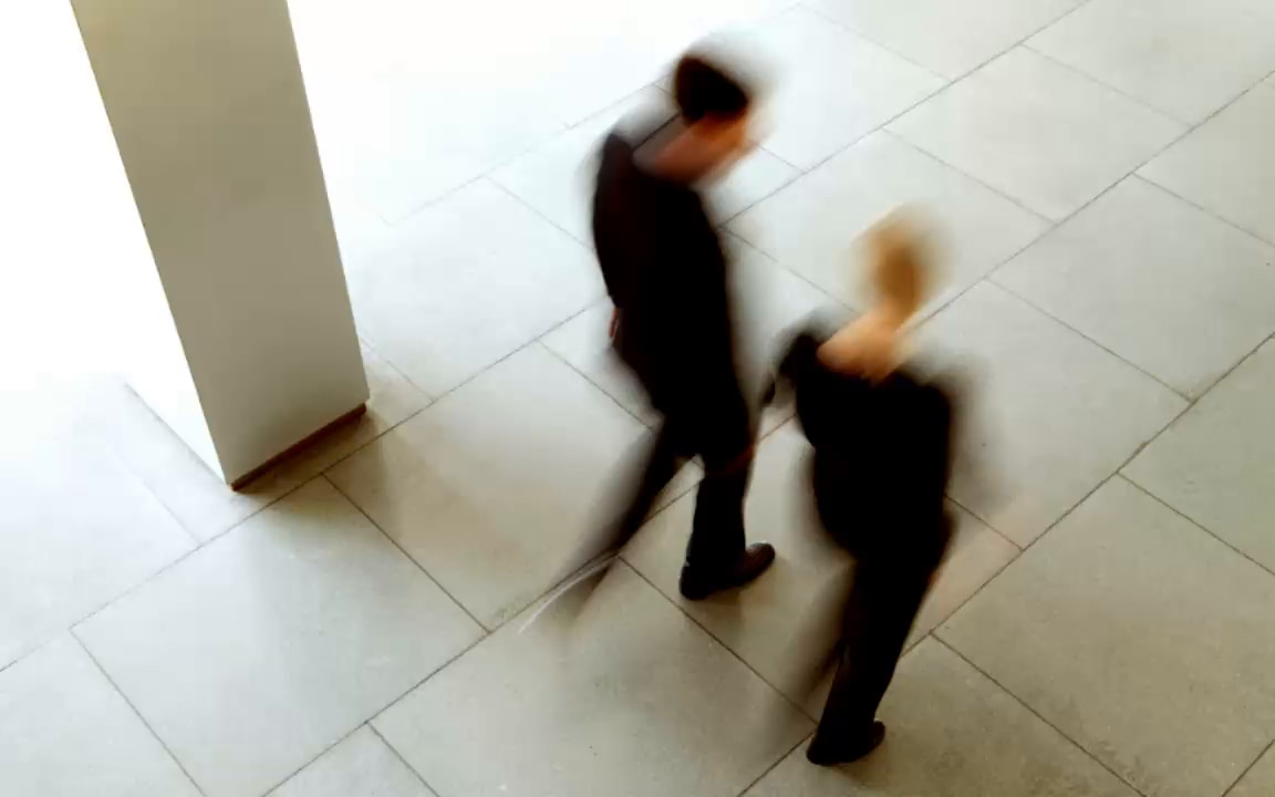Two colleagues in motion across a bright office floor, seen from above through refracted glass